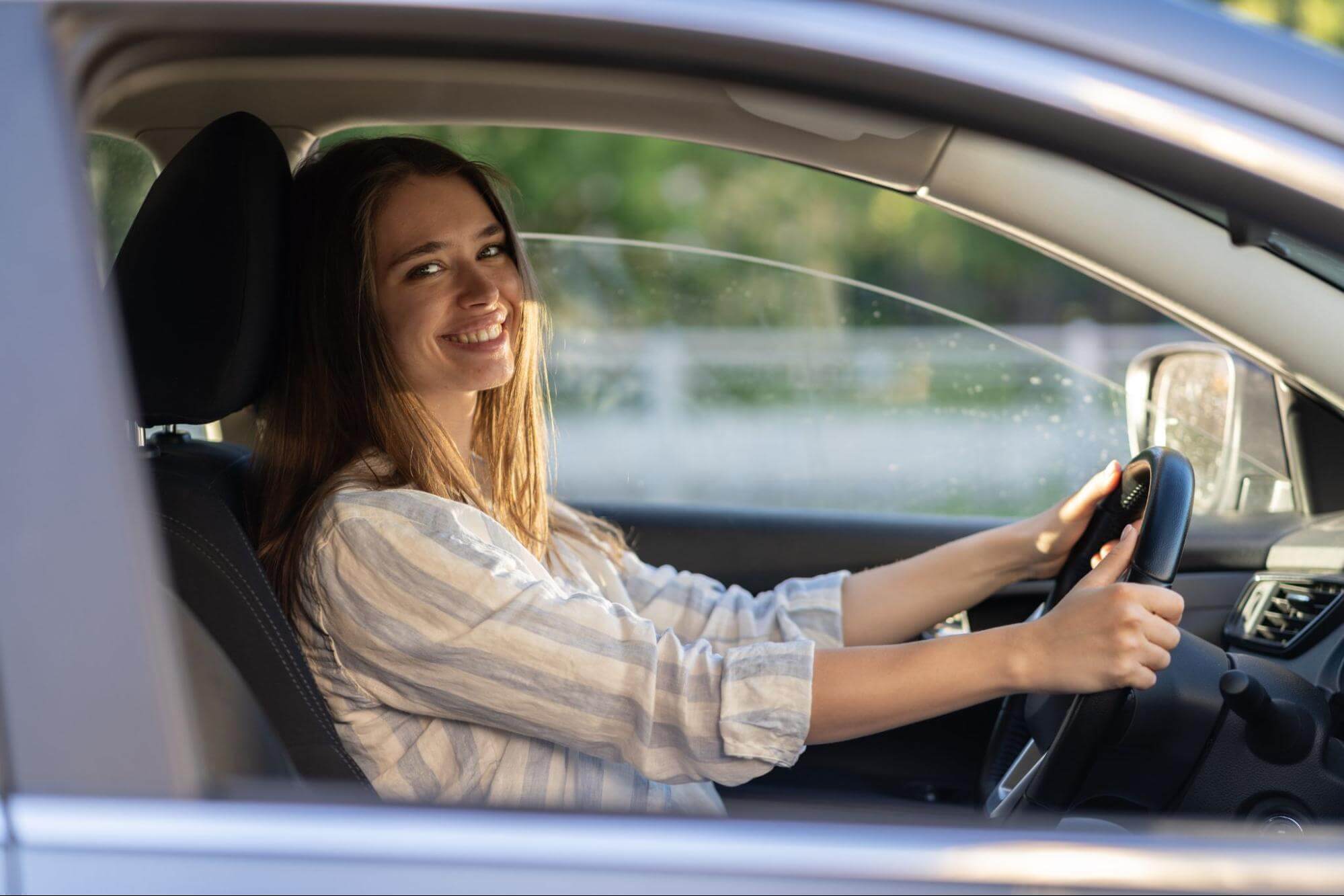 młoda, uśmiechnięta kobieta siedząca za kierownicą samochodu